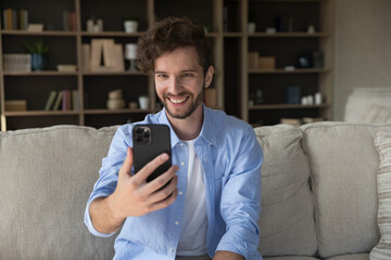 Happy millennial 35s guy staring at cell phone screen, enjoy videocall, on-line communication using modern tech and application, spend time alone at home, lead pleasant talk to family living abroad