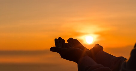 Silhouette of woman kneeling down praying for worship God at sky background. Christians pray to...