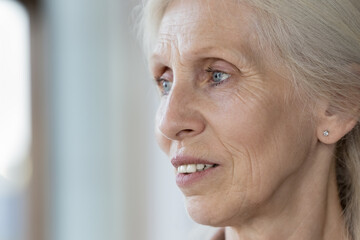 Close up face view of pensive elderly retired woman staring into distance, looks thoughtful, deep...