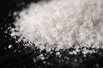 A heap of white salt crystals on a black stone background