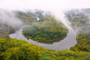 View from the treetop path to the Saar loop with rising clouds of fog on an autumn day