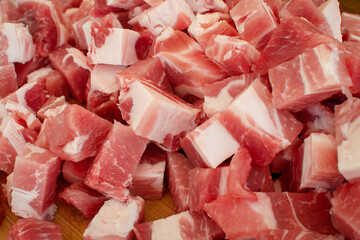Cubes of sliced raw meat on wooden cutting board closeup, selective focus