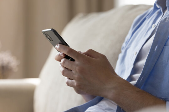 Cropped photo unknown male hands holding smartphone, read message on phone, browse news, chat on social media networks, texting, spend weekend time at home sitting on sofa. Modern technology, internet