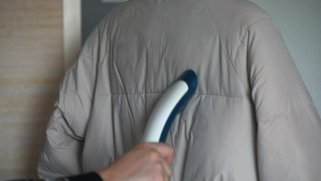 A person uses a steamer to steam a winter jacket, parka, or down jacket.