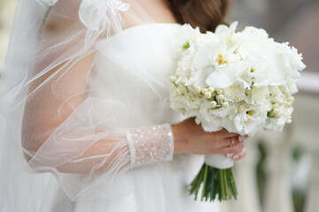 The bride is holding a beautiful white wedding bouquet in her hands. Wedding ceremony.
