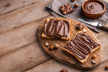 Board of bread with chocolate paste and hazelnuts on wooden background