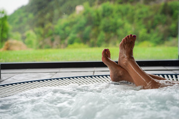 Feet in a jacuzzi in a winter scene in vacations in resort. Wellness and therapeutic relaxation in a spa in the mountains. - obrazy, fototapety, plakaty
