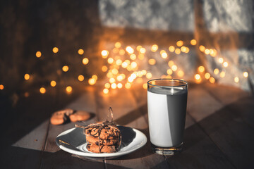 A stack of cookies and glass of milk for Santa on wooden background