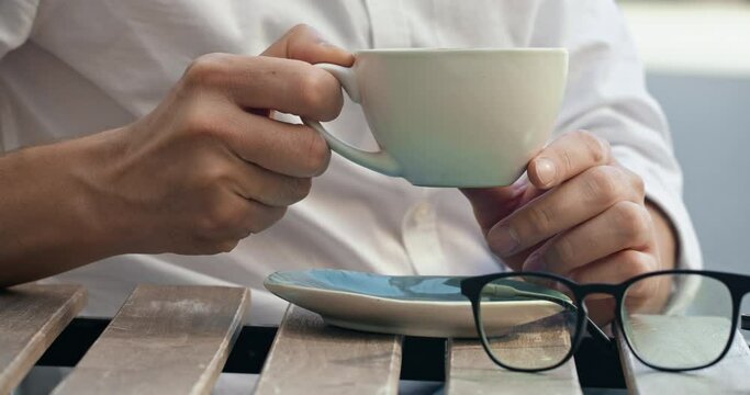Freelancer grabs mug of coffee during remote working outdoor. Remote worker entrepreneur sits at table sipping cup of hot coffee after work