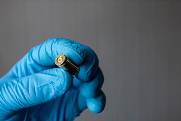 A criminologist, forensic medical expert holds a bullet casing in his hand at the crime scene. - obrazy, fototapety, plakaty