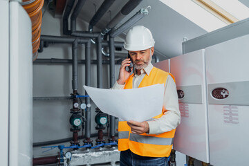 heating engineer checks modern gas heating system with a paper instruction at a boiler room. talk on mobile