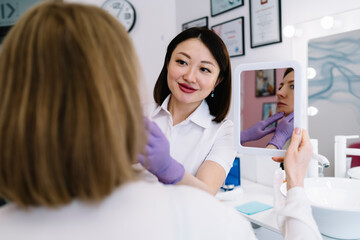 Positive Asian female cosmetician preparing patient for procedure