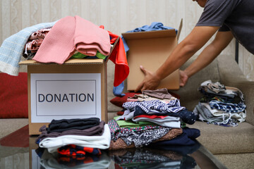 Asian woman putting used clothes into a cardboard box with other used clothes for donation, social...