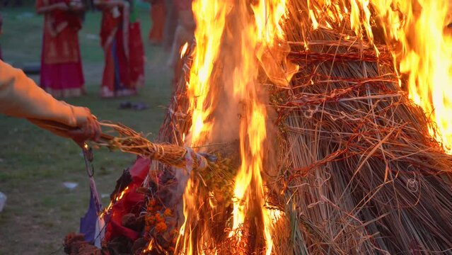 slow motion shot showing hand roasting wheat gram beans over fire on hindu festival of holi lohri with people dancing around a huge bonfire