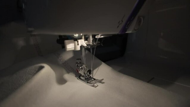 sewing machine working, needle stitches white fabric, close-up, slow motion