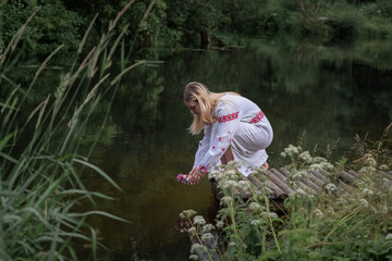 Fototapeta na wymiar A young beautiful blonde girl in a national costume in the river.