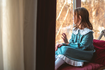 a pensive cute girl sits and looks out the window
