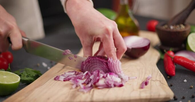 Woman cuts red Mars onion on wooden cutting board at domestic kitchen