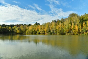 Fototapeta na wymiar La beauté bucolique des feuillage vert-dorés des arbres se reflétant dans les eaux de l'étang au domaine du château de la Hulpe 