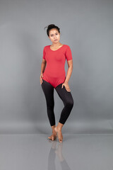 Healthy young woman in red t-shirt and black leggings doing yoga and stretching exercises isolated on grey background