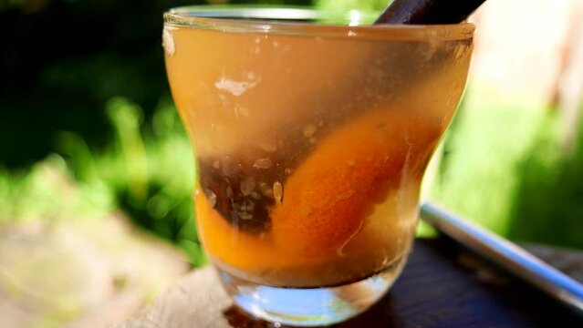  A tangerine caipirinha with cacha&ccedil;a (sugarcane liquor), sugar and ice cubes. Close-up shot of a Brazilian Caipirinha on the table, under the sun, in the backyard. Making a Caipirinha. Stirring drinks