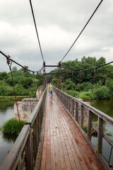 Fototapeta na wymiar A person traveling in the distance on a wooden suspension bridge in light summer rain, he is not in a hurry, the beauty and peace of nature