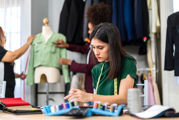Fototapeta premium Portrait of young beautiful woman fashion designer stylish sitting and working with color samples.Attractive young girl working with colorful fabrics at fashion studio.