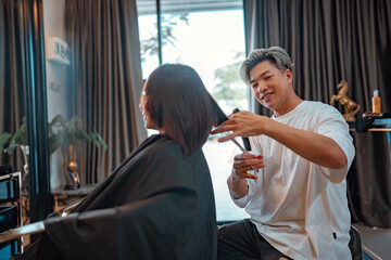 Asian woman getting haircut by hairdresser in the beauty salon, Man hairstylist trimming hair of...
