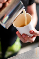 Professional barista hands pouring steamed milk into coffee paper cup making coffee.