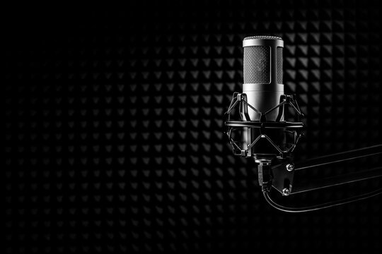 Professional microphone on the black sound proof panel. Recording studio, copy space.