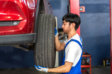 Professional car technician mechanic man in uniform work and maintenance repairing checking removing black wheel tire car before a long travel in auto service.Automobile service garage
