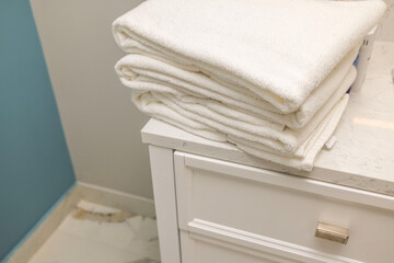 Close-up view of stack of towels on white nightstand in hotel bathroom. 