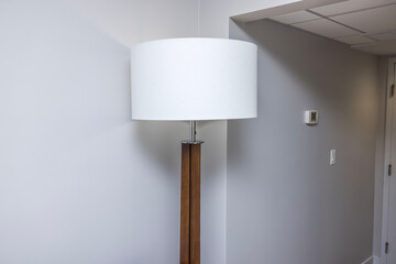 Close-up view of white floor lamp in hotel room on white wall background.