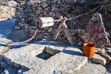 A primitive simple hand operated crank mechanism and a metal bucket over a square well opening, China