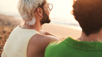 Close up, beautiful gay couple in love talking and laughing while sitting on the beach at dawn