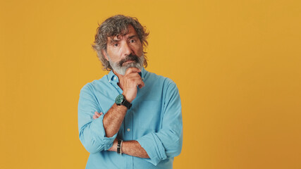 Fototapeta na wymiar Elderly gray-haired bearded man wears a blue shirt, looks at the camera listens carefully and agrees, isolated on an orange background in the studio