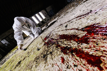 Scene of Crime Officer (SOCO) examines an area around some blood on a floor