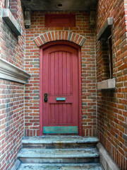 Red door in a recess to the rear of a brick building