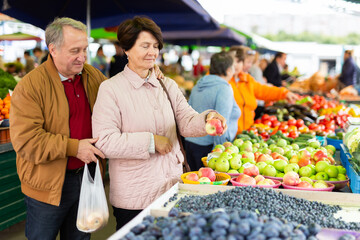 Elderly man and a woman buy apples at an open-air market