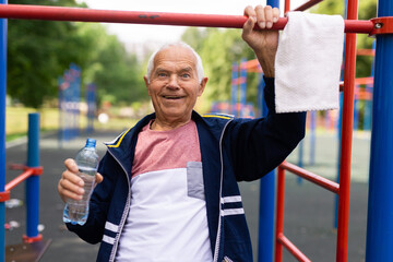 Fototapeta na wymiar Old man with bottle of water beside pullup bar outdoors