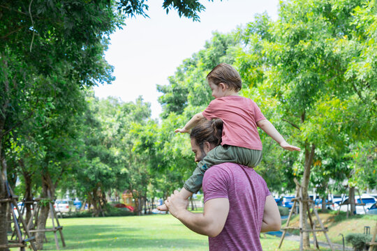 Cute little toddler boy sitting on father shoulder spinning around with happy and fun in park in summer holiday, smile Caucasian son and family laughing flying on sky bonding tenderness relationship