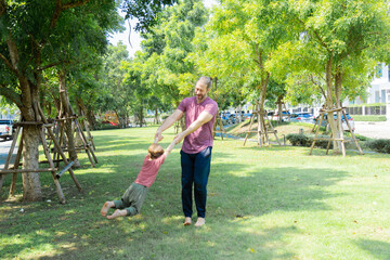 Cute little boy having fun jumping to the sky holding father's hands spinning around in park bonding relationship summer vacation, Caucasian family dad, and son relaxing playing together outdoors