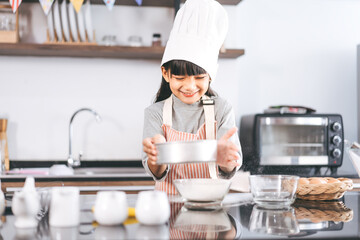 Little asian girl with chef hat and apron cooking in kitchen for homemade bake cake at home