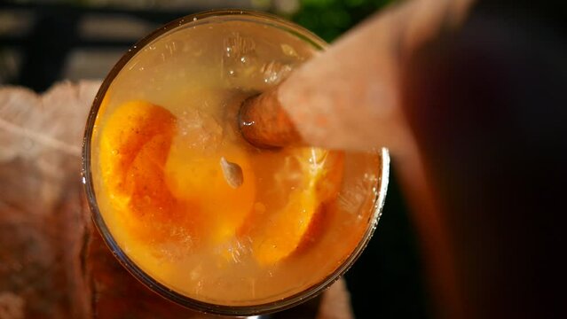 POV: a close-up shot of a person muddling a tangerine Caipirinha. Brazilian Caipirinha on the table. Stirring a Caipirinha cocktail. Using a wooden muddler. A tangerine caipirinha with cacha&ccedil;a liquor.