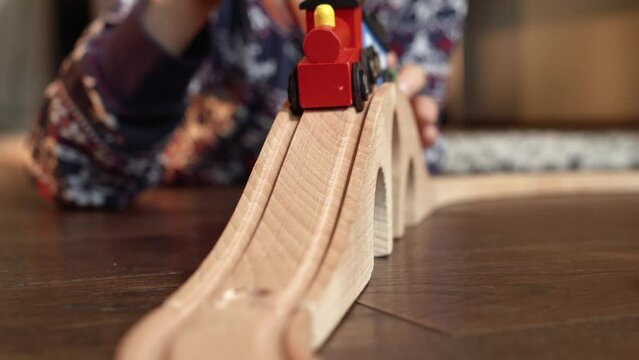 Closeup of little boy driving colorful train with hand while playing with wooden railroad on floor in living room