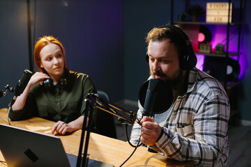 two radio hosts in headphones laughing while recording podcast in studio together.