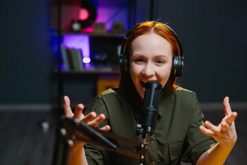 A girl in headphones speaks expressively into a microphone while recording a new blog episode.