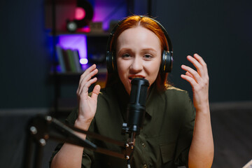 A girl in headphones speaks expressively into a microphone while recording a new blog episode.