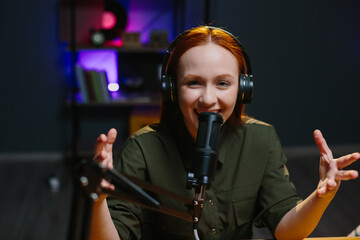 A girl in headphones speaks expressively into a microphone while recording a new blog episode.