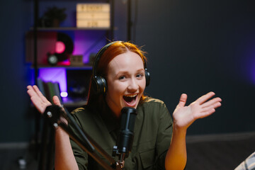 A girl in headphones speaks expressively into a microphone while recording a new blog episode.